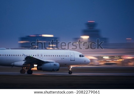 Airplane during take off on airport runway at night against air traffic control tower. Plane in blurred motion at night.