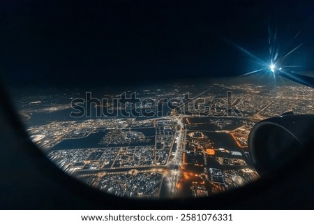 Airplane engine and wing flying over a big illuminated city at night, seen through an aircraft window