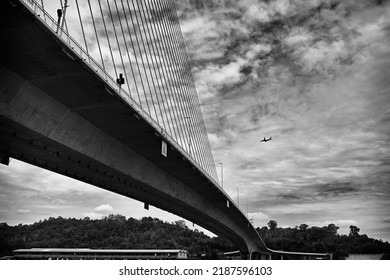 An Airplane Flies In The Sky Over Brunei Bridge.