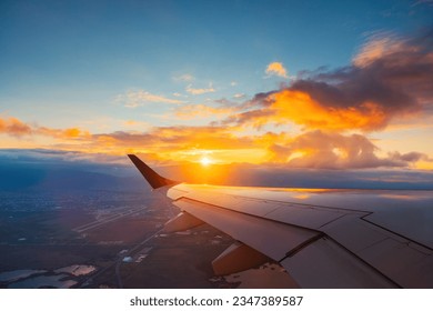 Airplane flight in sunset sky over city and wing of plane. View from the window of the Aircraft. Traveling in air. - Powered by Shutterstock