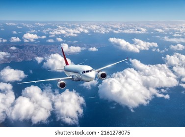 Airplane is flying above the clouds at in summer. Landscape with passenger airplane, mountains, blue sky, sea. Aircraft is taking off. Business travel. Commercial plane. Aerial view. Transport. Jet