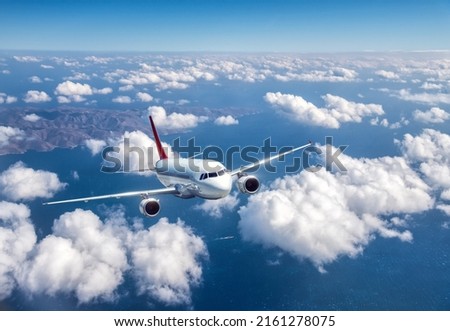 Airplane is flying above the clouds at in summer. Landscape with passenger airplane, mountains, blue sky, sea. Aircraft is taking off. Business travel. Commercial plane. Aerial view. Transport. Jet