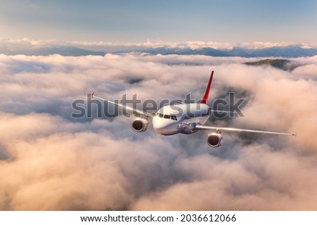 Airplane is flying above the clouds at sunrise in summer. Landscape with passenger airplane, beautiful clouds, mountains, sky. Aircraft is taking off. Business travel. Commercial plane. Aerial view 