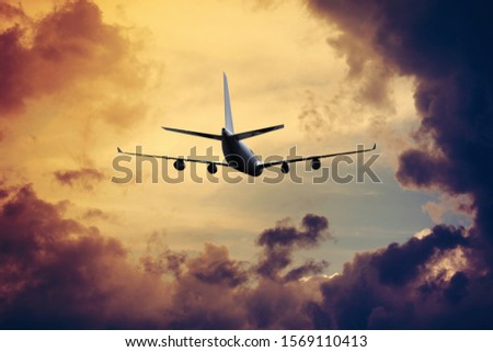 Airplane flying above dramatic clouds during sunset
