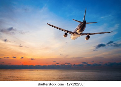 Airplane flying above tropical sea at sunset - Shutterstock ID 129132983