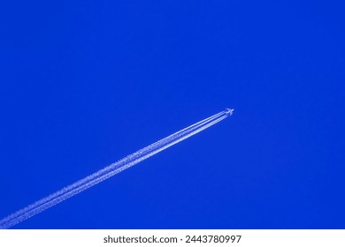 Airplane flying on deep cloudy blue sky with chemical direction trails, view from a distance