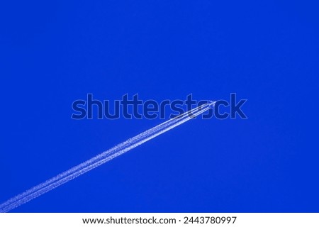 Airplane flying on deep cloudy blue sky with chemical direction trails, view from a distance