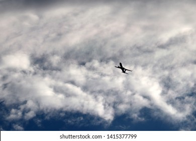 Airplane Flying In The Sky On Background Of Clouds. Silhouette Of A Commercial Plane During The Turn, Turbulence Concept