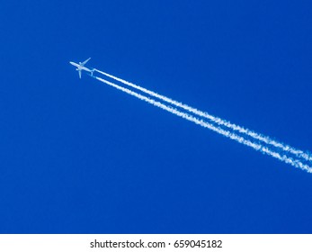 Airplane flying through clear blue sky with vapor trails
