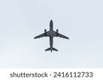 airplane flying through clouds (seen from below in dark silhouette against bright blue sky) shadow, outline of commercial airline plane seen from the ground