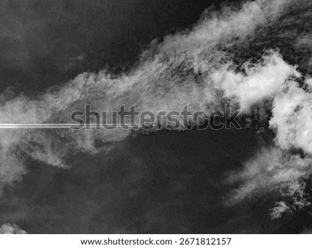 Airplane flying through dramatic clouds in monochrome sky
