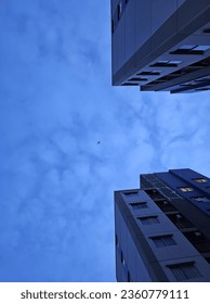 An airplane is flying through a gap between buildings with a cloudy blue sky.