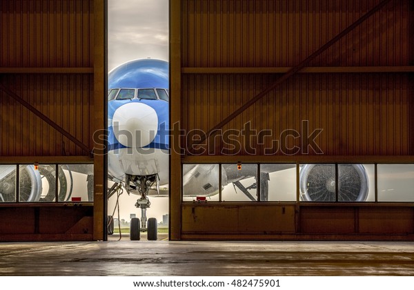 Airplane in front\
of half opened door to\
hangar