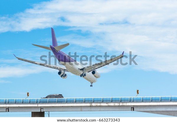 Airplane\
landing under blue sky over road bridge.\
