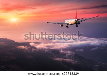 Airplane. Landscape with big white passenger airplane is flying in the red sky over the clouds at colorful sunset. Journey. Passenger aircraft is landing at dusk. Business trip. Commercial plane