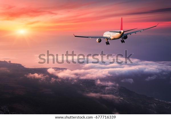 飛行機 大きな白い旅客機との風景が カラフルな夕焼けの雲の上を赤い空に浮かんでいます 旅 旅客機は夕暮れに着陸する 出張 商用機 の写真素材 今すぐ編集