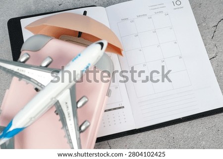 Airplane model on a suitcase with beach umbrella and planner. Concept of vacation planning, tourism, travel preparation, holiday booking and summer getaway.
