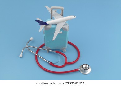 Airplane model on suitcase and red stethoscope on blue background. Travel insurance, medical tourism and healthcare concept.
