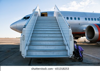 Airplane with a passenger boarding steps on the airport apron with a stroller prepared for the carriage of children