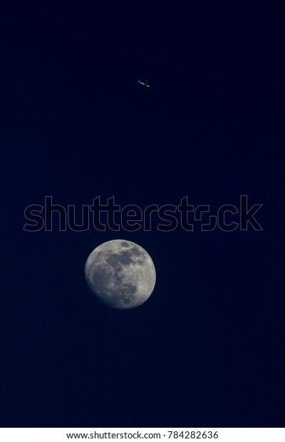 An airplane\
passing over the moon at\
nightfall