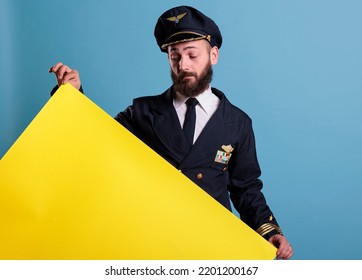 Airplane Pilot Holding Yellow Empty Advertising Banner With Copy Space, Aviator Looking At Blank Placard In Hands. Plane Captain In Uniform Standing With Promotion Ads Mockup