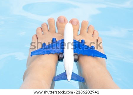 airplane plastic toy on woman feet against the pool water background.plane upside down isolated on grey background.fly invacation,book concept,travel,trip tourism agency.up in the sky,beautiful banner