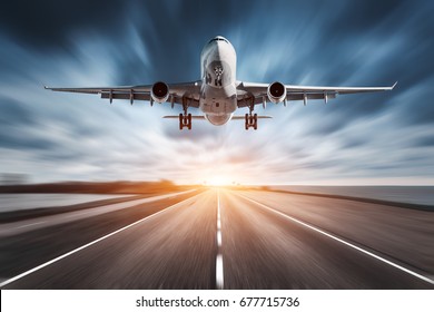 Airplane and road with motion blur effect at sunset. Landscape with passenger airplane is flying over the asphalt road and cloudy sky. Commercial plane is landing. Aircraft with blurred background 