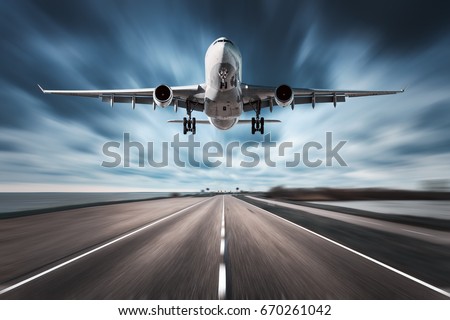 Airplane and road with motion blur effect. Landscape with white passenger airplane is flying in the cloudy sky over the asphalt road. Blurred. Passenger airplane is landing. Commercial plane. Aircraft