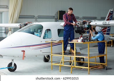 Airplane Service Crew Repairing Plane In Hangar:  Two Young Mechanics, Man And Woman, Repairing Jet Plane Turbine