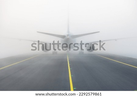 Airplane taxing on taxiway in white fog conditions. Yellow taxi line