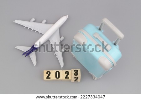 Airplane with travel suitcase and flipping numbers 2022 and 2023 on gray background. Tourism in new 2023 year.