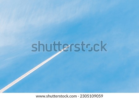 An airplane and a white trail from an airplane in a blue summer sky.airplane flying through blue sky with long vapor trails.Copy space.
