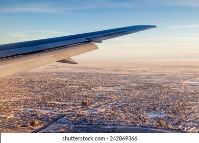 Airplane Window View Showing Wing Of The Plane Flying Over A Snow-covered City Of Calgary On A Sunrise Morning Just Prior To Touchdown.