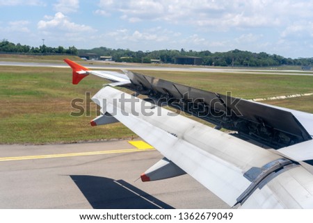 An airplane window view of wing and flaps after landing. Landing aircraft at the airport. Braking of the aircraft on the runway, wing of the plane is in working order. View from window. Close up shot