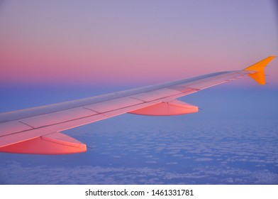 Airplane wing with the amazing vivid sunrise sky. Modern pastel peach and violet gradient made by nature. Relaxing view