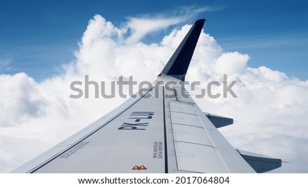 Airplane Wing in cloudy sky. Aircraft flying above the beautiful scenery of white fluffy clouds in the blue sky. Traveling by air POV shot. Air vehicle from the first person perspective