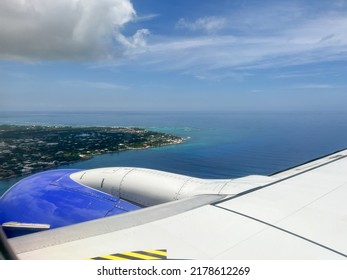 An Airplane Wing Flying Above The Clouds Over Cayman Islands On A Bright Blue Sky Sunny Day.