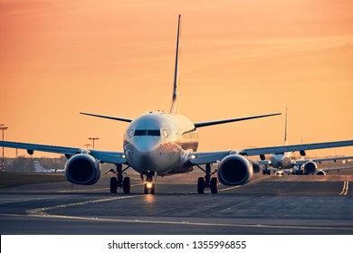 Airplanes In Row Taxiing To Runway For Take Off. Traffic At Busy Airpot At Sunset.