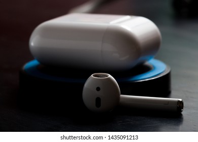 Airpod With Charging Case On A Wireless Charger In Low Key Lighting