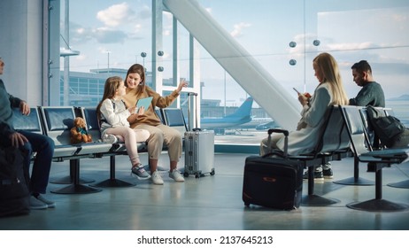 Airport Airplane Terminal: Cute Mother And Little Daughter Wait For Their Vacation Flight, Play E-Learning E-Educational Video Games On Digital Tablet. Young Family In Boarding Lounge Of Airline Hub