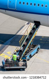 Airport Baggage Handler Placing Luggage On A Conveyer Belt To The Aircraft.