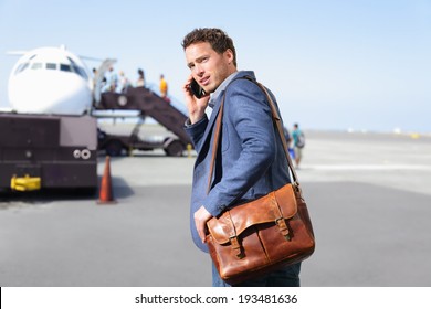 Airport Business Man On Smartphone By Plane. Young Male Professional Hip Businessman Talking On Smartphone Boarding Airplane Going Flying On Business Trip. Casual Male Wearing Suit And Laptop Bag.