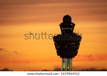 Airport control tower with a airplane landing in the background during sunset.