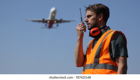 Airport Ground Worker Man Communicating Over Walkie Talkie With Air Traffic Control About Airspace Security Using Telecommunication Equipment While Airplane Flying Over Head