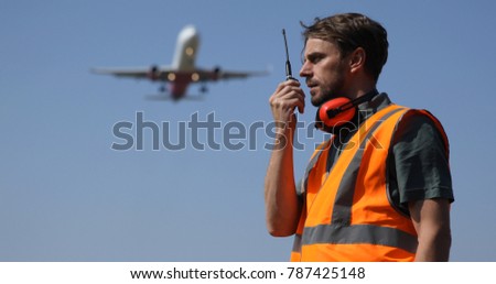 Airport Ground Worker Man Communicating Over Walkie Talkie with Air Traffic Control about Airspace Security Using Telecommunication Equipment while Airplane Flying Over Head
