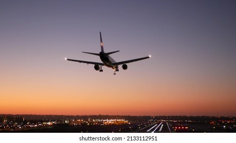 Airport runway lights at night, plane or airplane landing to airstrip, twilight dusk and sunset. Airliner jet arriving to aerodrome, San Diego airfield, California USA. Aircraft flying mid air in sky.