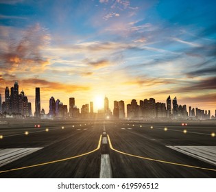 Airport runway with modern skyscrapers silhouettes on background in beautiful sunset light. Cloudy sky and sun rays. Travel and cities concept