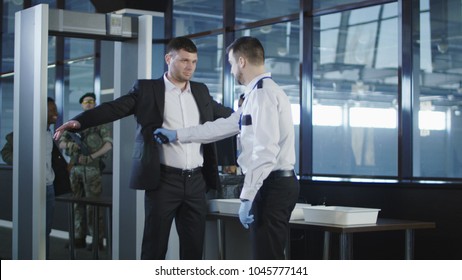 Airport Security Agent Using A Metal Detector On A Male Passenger In A Suit To Pat Him Down At The Boarding Gate After Passing Through The X-ray Scanner.