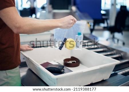 Airport security check before flight. Passenger holding plastic bag with liquids above container personal items. 