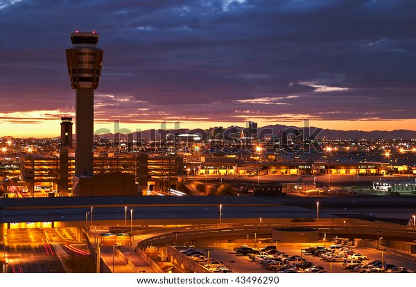 Airport at sunset with\
lit city skyline.